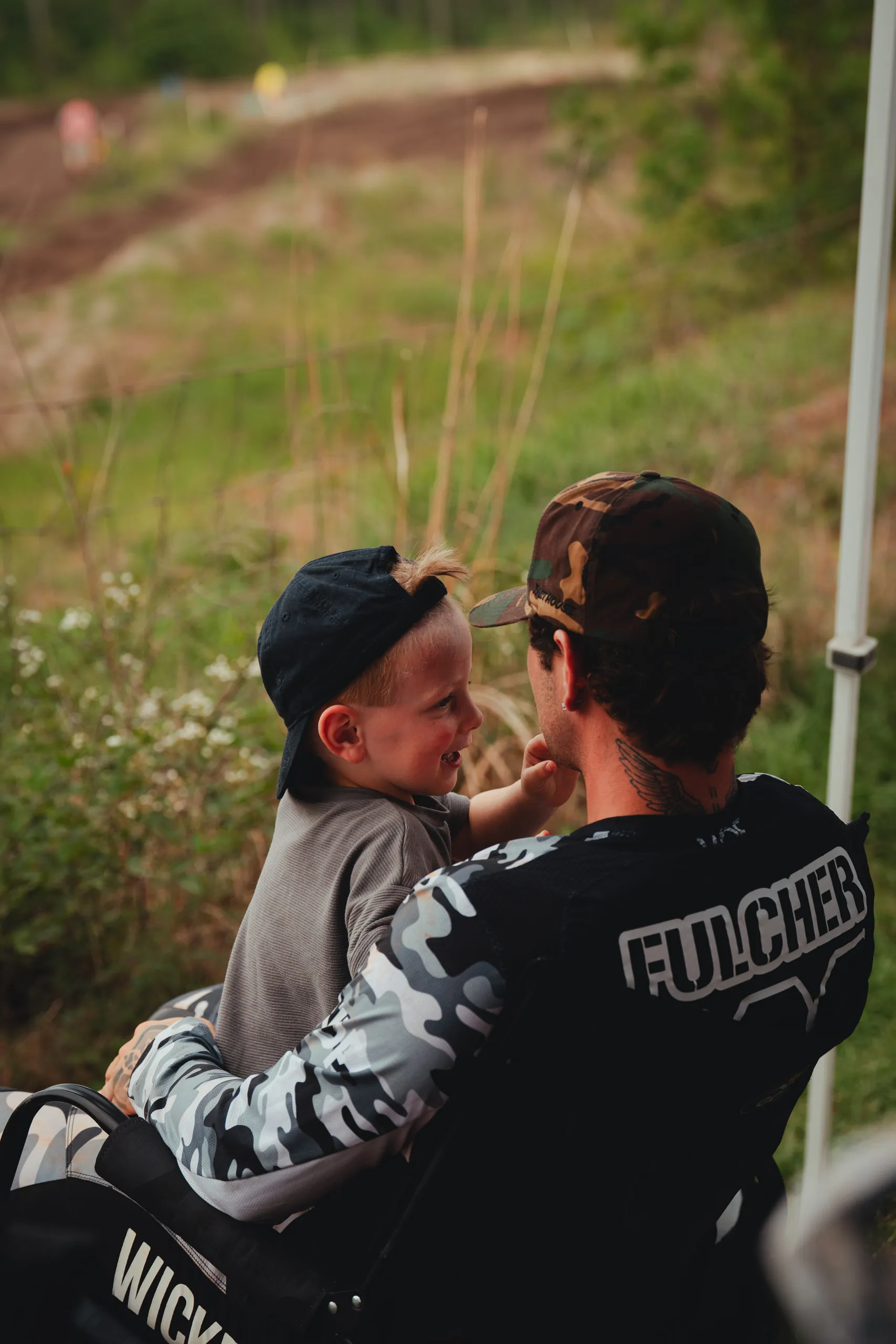 A young boy leans in close to a rider in a Fulcher jersey beside the track