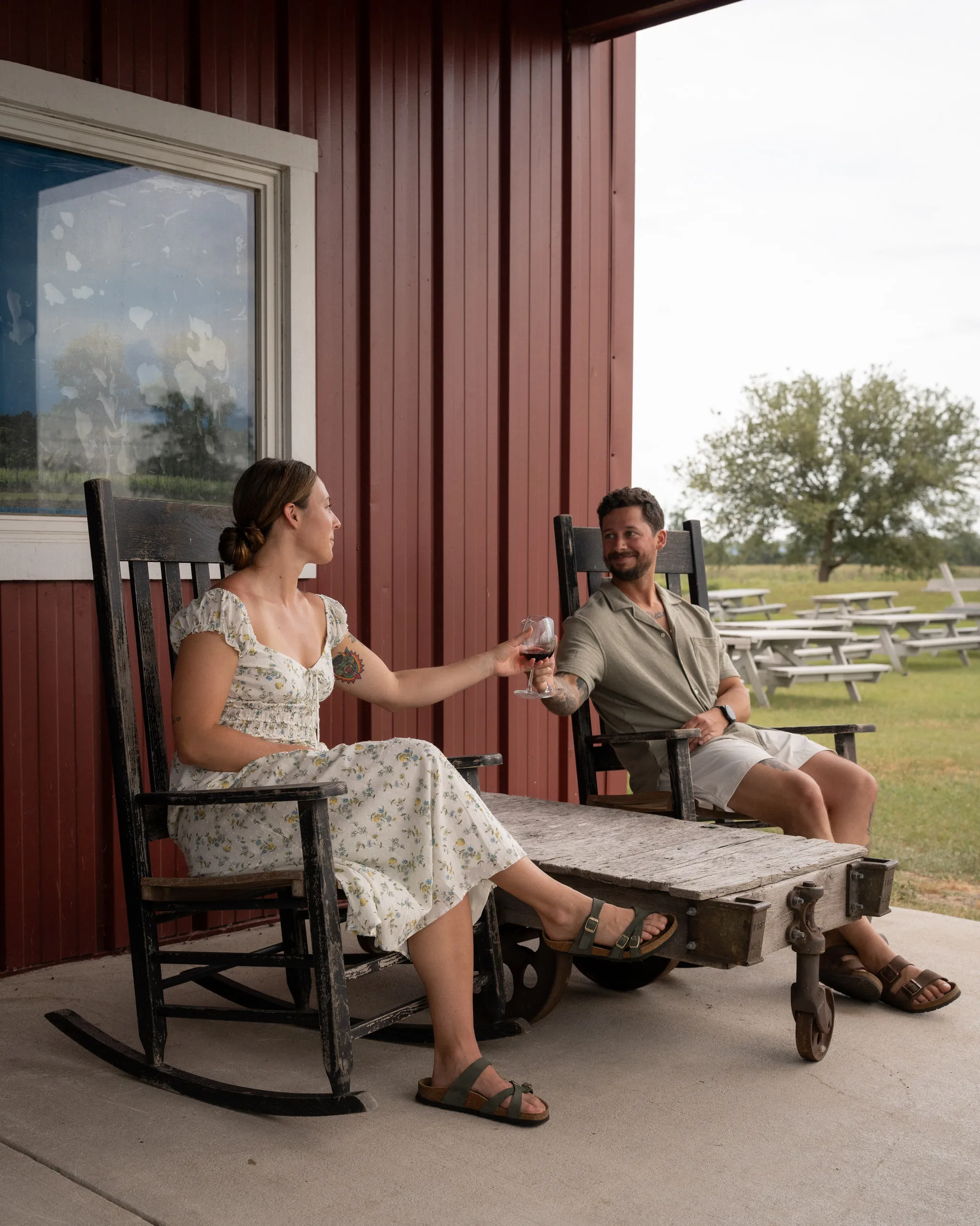 A couple relax with drinks in rocking chairs on a red-walled porch