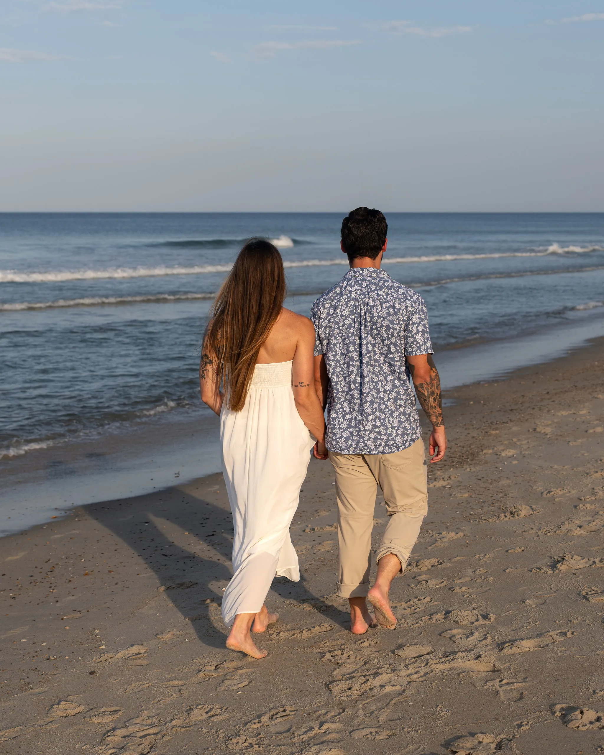 A couple walk hand in hand along the waterline on an empty beach
