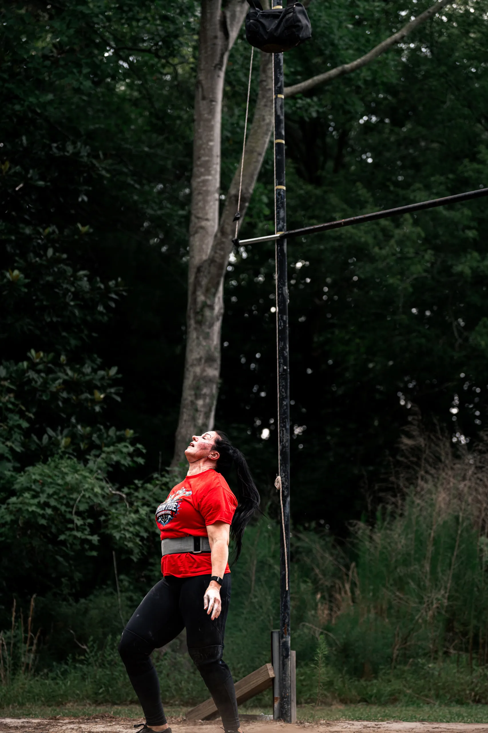 A competitor in a red shirt watches a weight sail over the height bar overhead