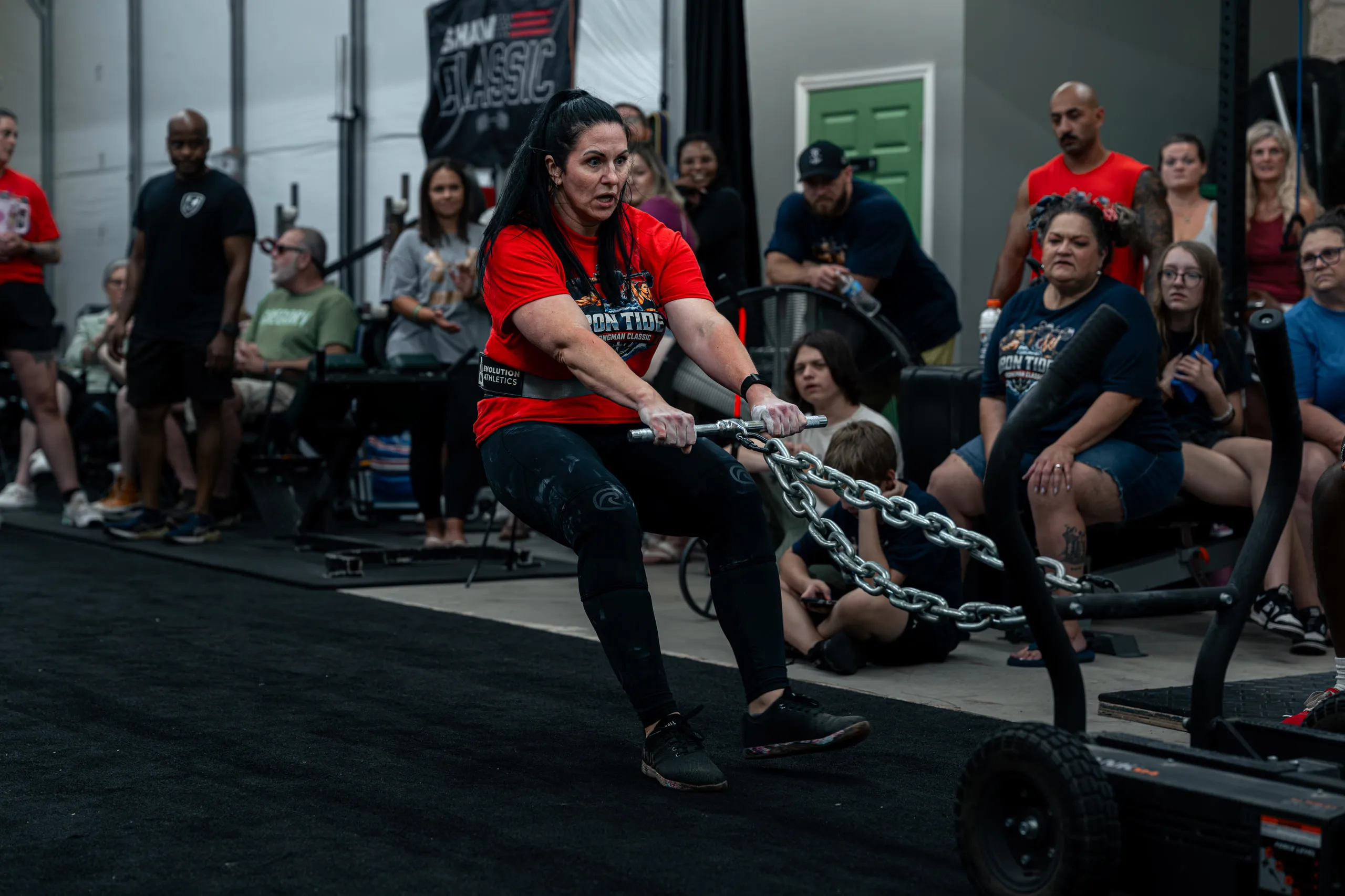 A competitor drags a chained sled across the gym floor as the crowd watches from both sides